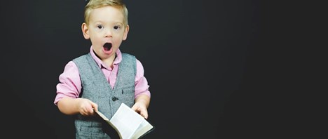 Child in grey vest with pink short holding book